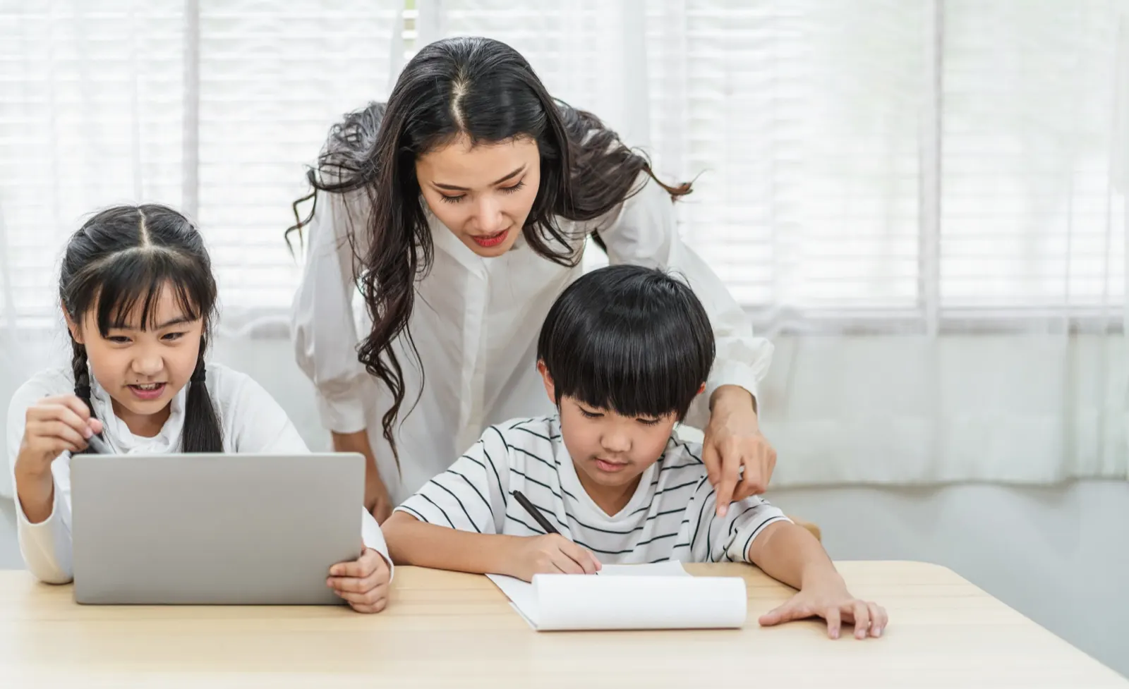 ノートパソコンで勉強する姉弟と、うしろから見守る母親