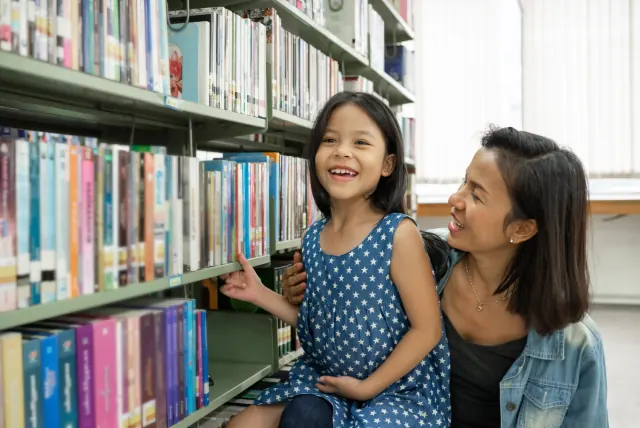 学校の図書室の本棚の前で笑う母親と娘