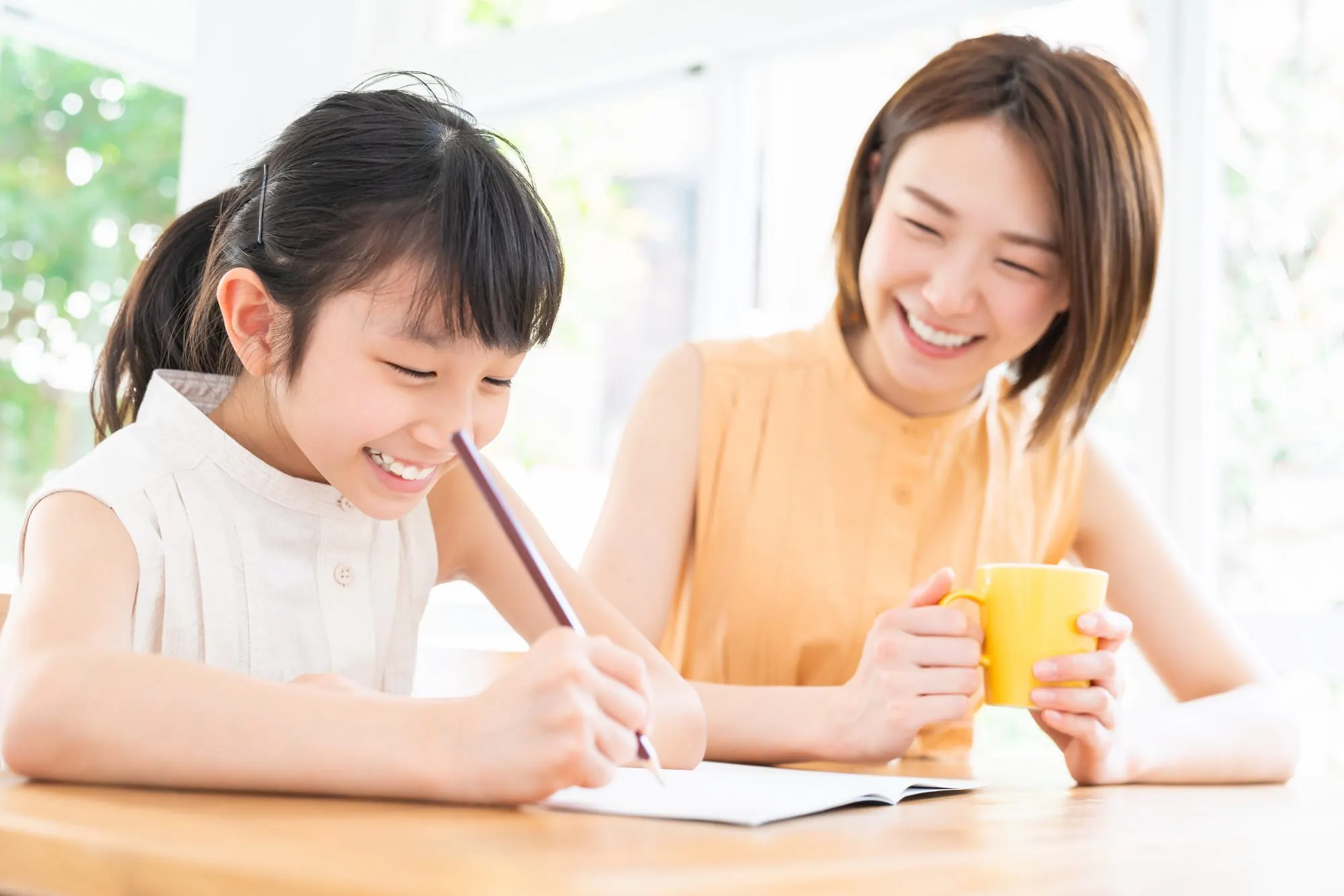 ノートに書き込む娘と、となりで笑って見守る母親