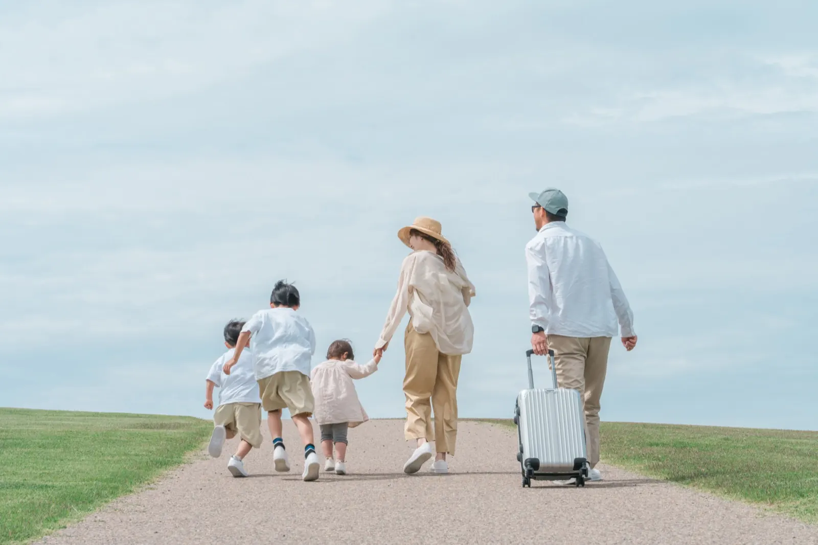 スーツケースを引いて空の下を歩く家族