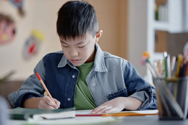 自宅の机でノートに書き込みながら勉強する中学生くらいの男の子